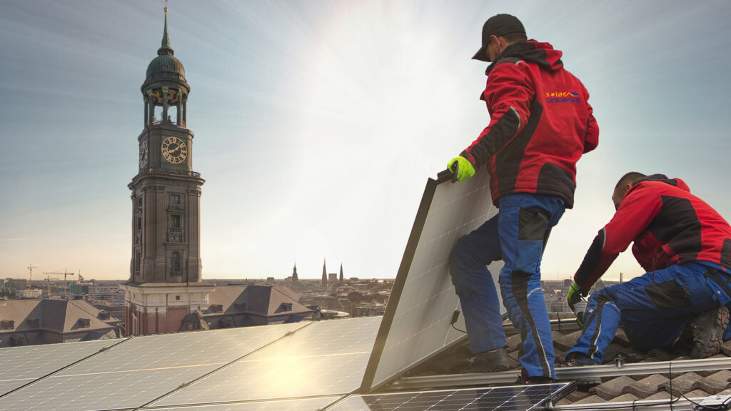 Bild mit zwei Handwerkern, die Solarmodule montieren. Im Hintergrund ist ein Kirchturm.